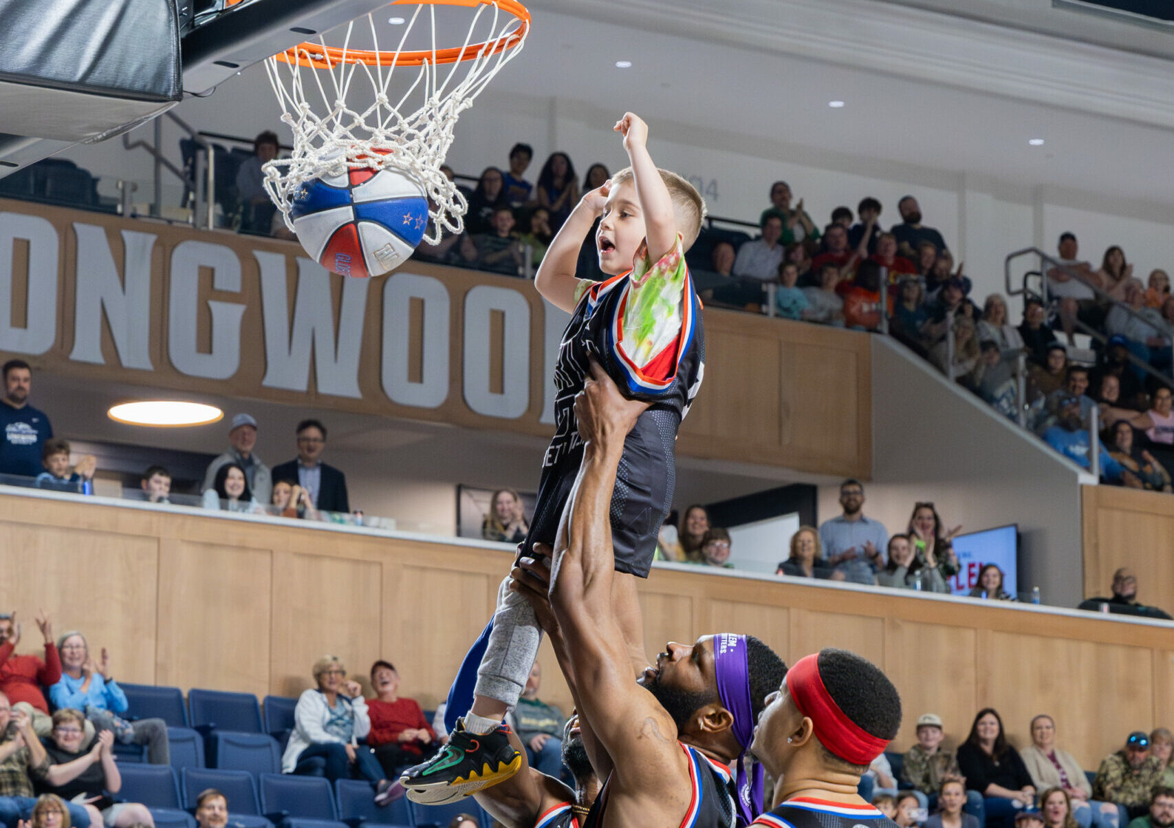 Young fan is assisted by Globetrotter to execute a dunk.