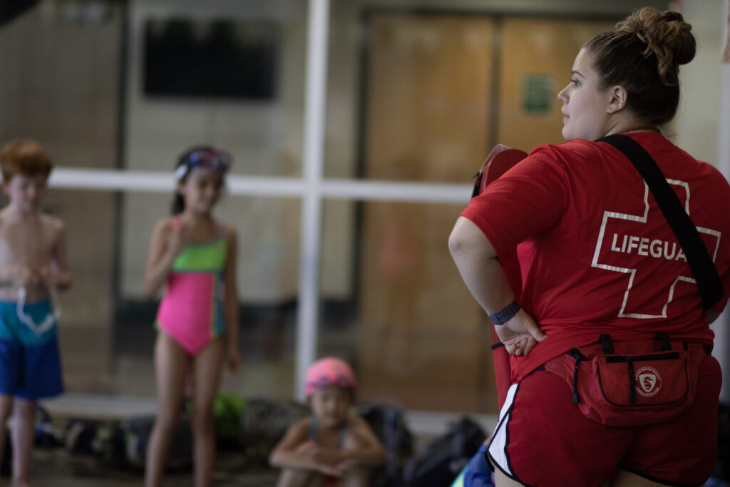 Lifeguard supervising children jumping into an indoor pool at a campus recreation center