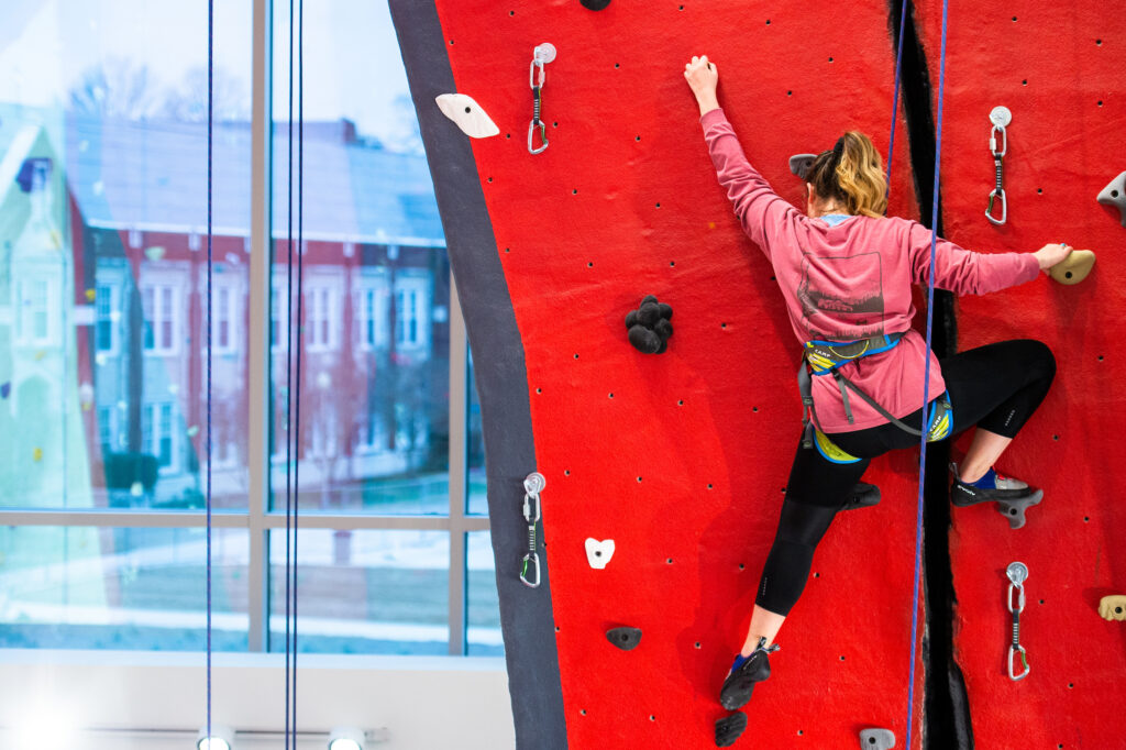 Student climbing indoor rock wall at university recreation center campus life program.