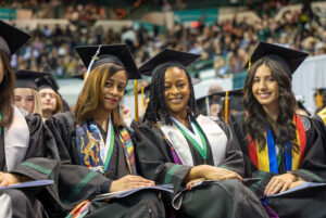 Three Cleveland State University graduates sit together during commencement, celebrating the milestone with classmates.