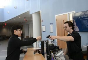Santiago Contreras sets up a shot with a student actor scanning a membership card at the Harper College Recreation desk for the onboarding video series.