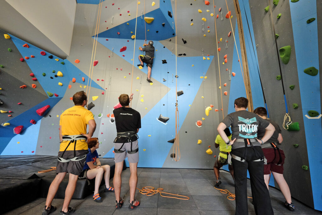 College students participate in outdoor recreation near a climbing wall, highlighting campus recreation center planning and student engagement.
